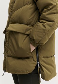 Olijfgroene pufferjack met een gequilt ontwerp, voorzien van een voorzak, elastische manchetten en zijritsen voor verstelbaarheid.
