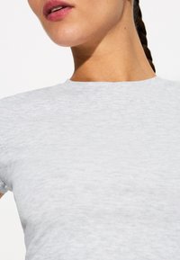 Tricou scurt din material moale, de culoare gri deschis, cu mâneci scurte, guler rotund clasic, textură netedă și detalii de design minimaliste.