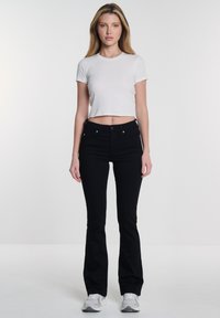 Jeans negros de campana con una cintura ajustada, combinados con una blusa corta blanca de manga corta. El conjunto presenta un diseño limpio y minimalista.