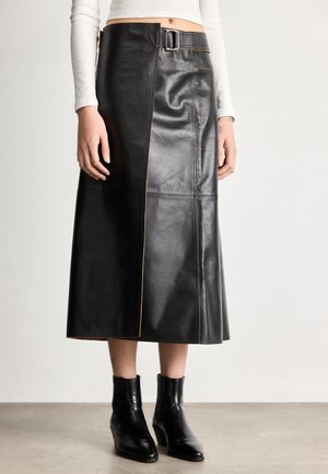 Czarna skórzana spódnica midi o prostym kroju, z kontrastowym przeszyciem, z przodu z klamrą oraz kieszeniami w bocznych szwach. Czarne botki za kostkę.