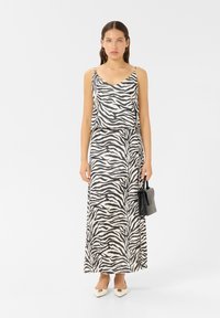 Schwarzes und weißes Zebramuster-Kleid, ärmellos mit V-Ausschnitt, fließendes Maxikleid, kombiniert mit einer kleinen schwarzen Tasche und weißen Absatzschuhen.