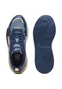 Les baskets Puma présentent un upper en mesh bleu marine avec des accents bordeaux, un talon beige rembourré et une semelle en caoutchouc texturé pour une meilleure adhérence.