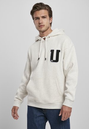Lys grå hettegenser laget av mykt stoff, med en frontlomme, snor i hetten, og et svart "U" og nummer "05" lapp på venstre bryst.