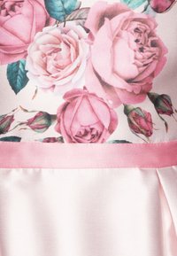 Blommig klänning med rosa rosor och gröna blad på en mönstrad överdel, kompletterad med en enfärgad ljusrosa satinkjol.