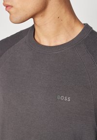 Grå strikket genser med rund hals og ribbestruktur. Subtil "BOSS"-logo i lysegrått på forsiden.