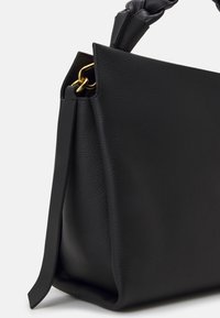 Sort læder håndtaske med en struktureret overflade, flettet håndtag, guldfarvet hardware og et veludformet design. Har en flad bund for stabilitet.