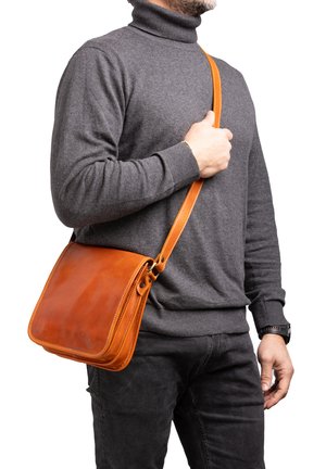 Borsa a tracolla in pelle marrone con forma rettangolare, cuciture abbinate e una larga tracolla regolabile, indossata da una persona con un dolcevita grigio.