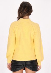 Gelbes gestricktes Sweater mit weicher Textur, rundem Ausschnitt und puffigen Ärmeln, kombiniert mit einem schwarzen, gerafften Minirock.