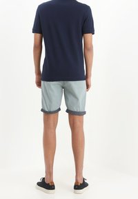 Navy blue polo shirt, light blue rolled shorts, and black shoes. Fabric appears smooth, with a classic design and subtle accents.