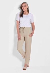 Beige, lichtgewicht, taps toelopende broek met een elastische tailleband en koord. Gepaard met een eenvoudige witte shirt met korte mouwen. Eenvoudig ontwerp.