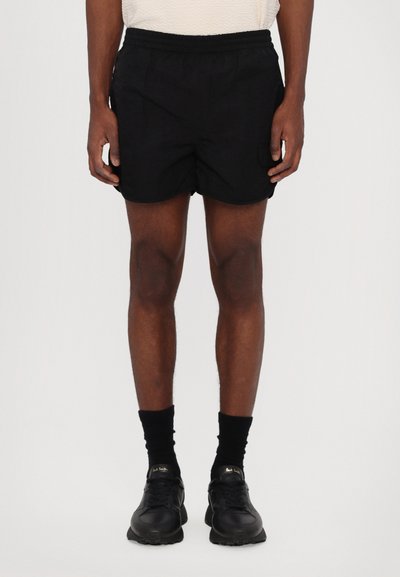 Schwarze Shorts mit einem elastischen Bund, seitlichen Taschen und einer glatten Textur. Getragen mit schwarzen Socken und Turnschuhen, die einen lässigen Look präsentieren.