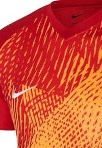 Maglietta sportiva Nike rossa e arancione con scollatura a V, caratterizzata da una texture a motivo dinamico e un logo bianco sul lato sinistro.