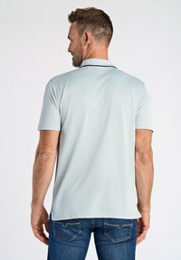 Ljusblå pikétröja med en kontrasterande mörk krage, korta ärmar och ett subtilt strukturerat tyg, bärs med mörkblå jeans.