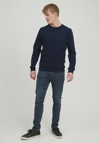 Hanorac din bumbac de culoare bleumarin, cu guler rotund, manșete și tiv cu dantelă, asortat cu blugi skinny de culoare bleumarin închis și adidași negri.