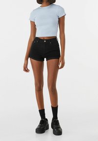 Top corto ajustado de color azul claro combinado con pantalones cortos de mezclilla negros. El conjunto incluye dobladillos doblados, bolsillos delanteros y zapatillas negras gruesas con calcetas.