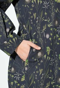 Dunkel gefüttertes Kleid mit floralem Muster, das grüne und weiße Pflanzenmotive zeigt, mit einer seitlichen Tasche und gerafften Details an der Taille.