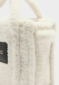 Borsa in peluche bianco con una superficie morbida e Texturata, con una base in pelle nera e un piccolo logo decorativo. Manici spessi e resistenti.