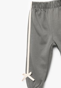 Szare dziecięce spodnie z elastycznym pasem, kontrastującymi kremowymi paskami po bokach i dekoracyjną kokardką przy kostce. Miękka tkanina, luźny krój.
