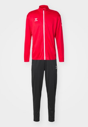 Rode trainingsjack met een witte rits, lange mouwen en logo; gecombineerd met zwarte trainingsbroek met een soortgelijk logo.