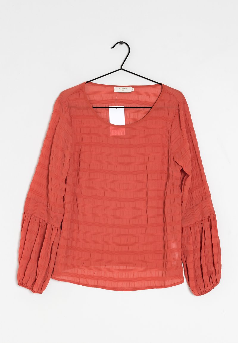 Blouse corail avec un col rond, motif à carreaux texturé, manches évasées et poignets élastiques. Tissu léger et semi-transparent.