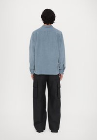 Light blue button-up shirt with long sleeves, back pleat, and dark cargo pants featuring side pockets and a relaxed fit.