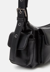 Coin de sac à main en cuir noir avec bandoulière réglable et boucle argentée, présentant deux petites poches avant à rabat avec des détails de couture.