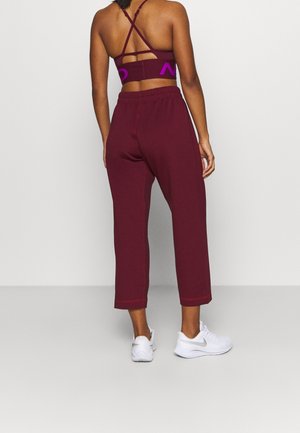 Joggers courts bordeaux avec des détails cousus, assortis à un soutien-gorge de sport à dos croisé et logo en violet.