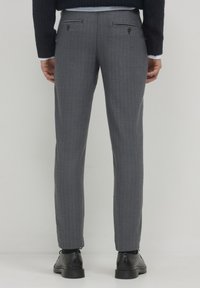 Pantaloni grigi a spina di pesce con taglio slim, dotati di due tasche posteriori con bottone, indossati con scarpe nere e un maglione blu navy.