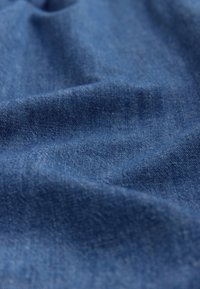 Džinso audinys gilios mėlynos spalvos su matoma tekstūra ir minkšta, šiek tiek raukšlėta paviršiaus struktūra, pasižymi lygiu paviršiumi ir smulkia pynimo rašto faktūra.