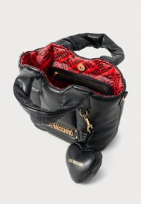 Bolsa preta acolchoada com um interior padronizado em vermelho, ferragens douradas e um charme destacável em forma de coração preto rotulado "LOVE MOSCHINO."