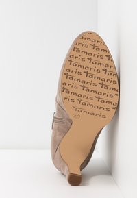 Botte à talons en daim beige pour femmes, montrant la semelle avec le logo "tamaris" répété et la taille 37 embossée sur la semelle.