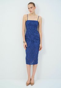 Robes midi en dentelle bleue avec des bretelles fines, arborant des motifs floraux complexes et une silhouette ajustée, accompagnées de talons hauts neutres.