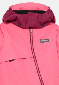 Ružová zimná bunda s vínovou kapucňou, obsahujúca predný zips, patentky a nášivku s logom na hrudi. Hladký, vodeodolný materiál.