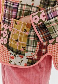 Prošívaná bunda s kombinovanými květinovými a kostkovanými vzory v růžové, zelené, hnědé a žluté barvě, s růžovým lemováním a kapsou s detailem oka.