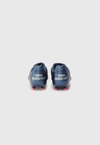 Chaussures de football avec un dessus synthétique bleu marine foncé, présentant le logo "New Balance" en blanc et des accents rouges sur le talon et les crampons.