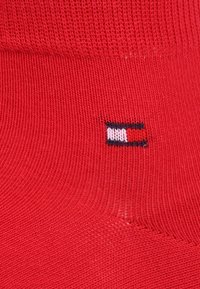Chaussettes en coton rouge avec un logo tissé en bleu, blanc et marine sur le côté, affichant une texture côtelée sur toute leur surface.