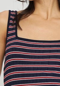 Femme portant un haut sans manches bleu marine avec des rayures horizontales rouges et blanches et un décolleté carré.