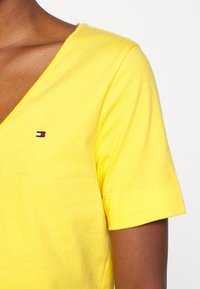 Camiseta amarilla de cuello en pico fabricada en suave algodón. Presenta mangas cortas y un pequeño logotipo bordado en rojo, blanco y azul en el pecho.