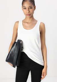 White sleeveless tank top in soft fabric, paired with a sleek black leather bag featuring round handles and visible stitching details.