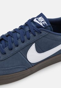 Jūrų laivyno suknelės sportbačiai su balta Nike swoosh, tekstūruota pilka sola ir atitinkančiomis raištelėmis. Liežuvėlyje yra prekės ženklo logotipas. Žemas profilis.