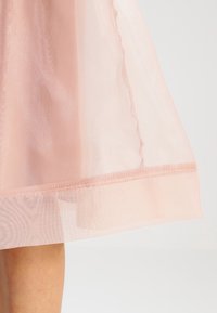 Transparent rosa kjol med ett flödande mönster, som har delikata volanger längs fållen och en subtil textur. Tyget verkar lätt och mjukt.