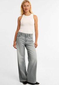 Lichtgrijze wijde spijkerbroek gemaakt van denim met vijf zakken, knoopsluiting en een gladde textuur; gecombineerd met een aansluitend wit tanktop.