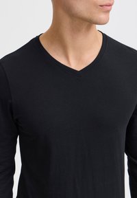 Tricou negru cu mânecă lungă și decolteu în V, confecționat dintr-un material neted, având un design ajustat cu detalii subtile de cusătură pe guler.