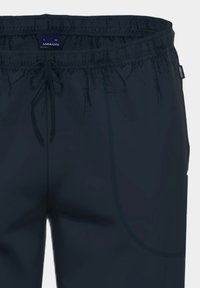 Hose mit elastischem Bund in Marineblau, ausgestattet mit einem Zugband, einer Seitentasche und einer glatten, glänzenden Textur. Markenetikett innen sichtbar.