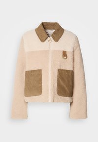 Veste en fausse fourrure avec un corps crème, un col en velours côtelé marron et deux poches plaquées. Elle possède une fermeture éclair à l'avant et un accent en métal.