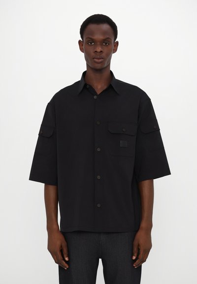 Fekete, rövid ujjú, gombos ing. Két elülső zsebbel, galléros kivitelben és textúrált anyagból készült. Tiszta, modern fazon, diszkrét márkázással.
