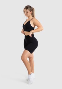 Zwart sportbeha en high-waisted shorts gemaakt van rekbaar materiaal. Heeft een aansluitend ontwerp en een gladde textuur. Gecombineerd met witte sportschoenen.