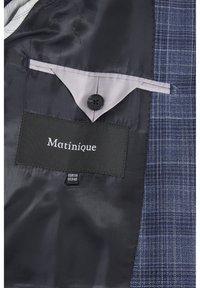 Inredningen av en marinblå kostymjacka med ett strukturerat mönster, satinfoder, en ficka med knäppning och en etikett som säger "Matinique" med storleksinformation.