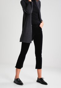 Pantalons cropped noirs, cardigan côtelé gris foncé, et chaussures noires. Le cardigan a une ouverture à l'avant ; les pantalons sont ajustés avec une légère évasement à l'ourlet.