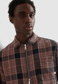 Marynarka w kratę z różowo-granatowym wzorem, z zapięciem na zamek błyskawiczny i kołnierzem, wykonana z teksturowanej tkaniny.